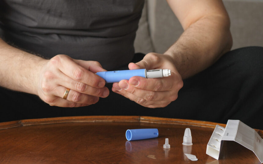 Man sitting in front of coffee table preparing Semaglutide Ozempic injection.