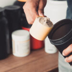 Hands holding scoop of protein powder and shaker