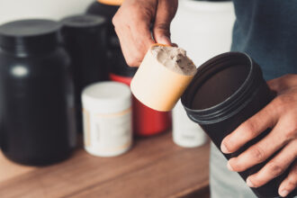 Hands holding scoop of protein powder and shaker