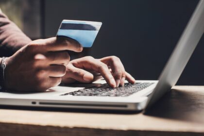 unseen person holds credit card while typing on a laptop