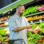 Man uses phone in produce section at grocery store to get more information about his purchases.