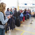 female traveller texting at airport check-in desk