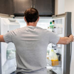 Back of man looking into open fridge deciding what to eat