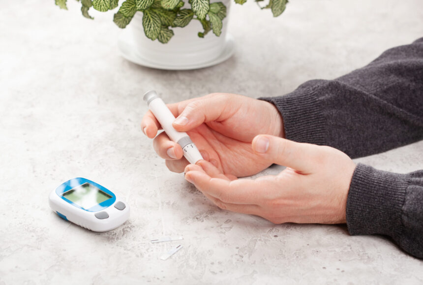 Man hands using lancet on finger to check blood ketone level. The meter is on the table nearby.