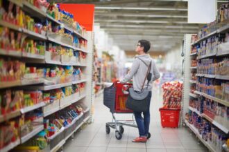 Person standing in grocery store aisle pushing a shopping cart.