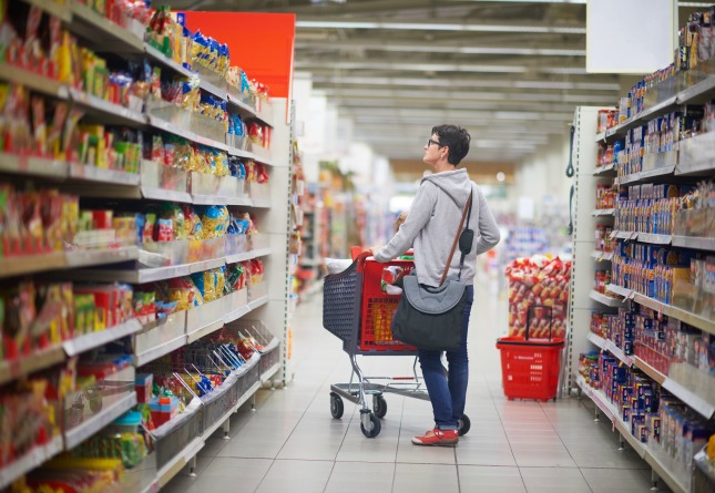 Person standing in grocery store aisle pushing a shopping cart.