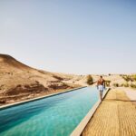 Wide shot of man walking around edge of pool at Moroccan desert camp