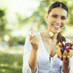 Woman holding a cantaloupe bowl with berries inside smiling into camera.