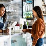 Young woman using credit card reader at coffee shop counter