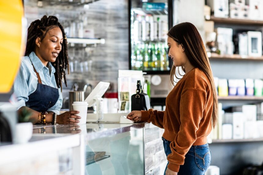 Young woman using credit card reader at coffee shop counter