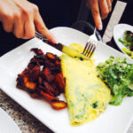 Cropped image of woman having spinach feta omelette served with bacon