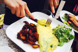 Cropped image of woman having spinach feta omelette served with bacon