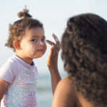 Mother applying sun protection sunscreen on her baby girl's face.