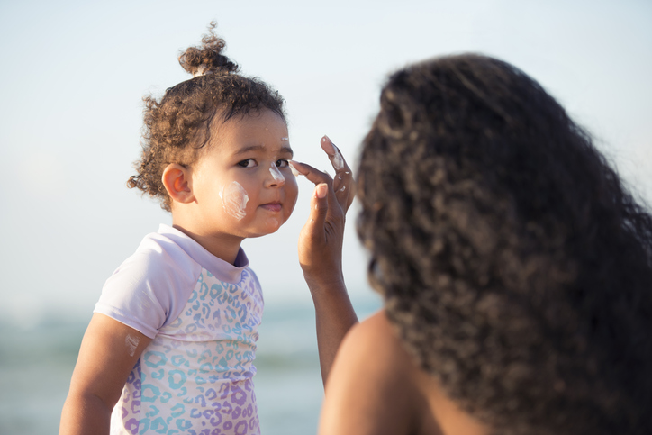 Mother applying sun protection sunscreen on her baby girl's face.