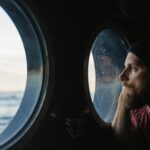 Man at the porthole window of a vessel sailing the ocean