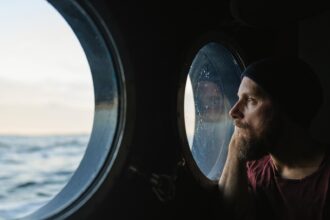 Man at the porthole window of a vessel sailing the ocean