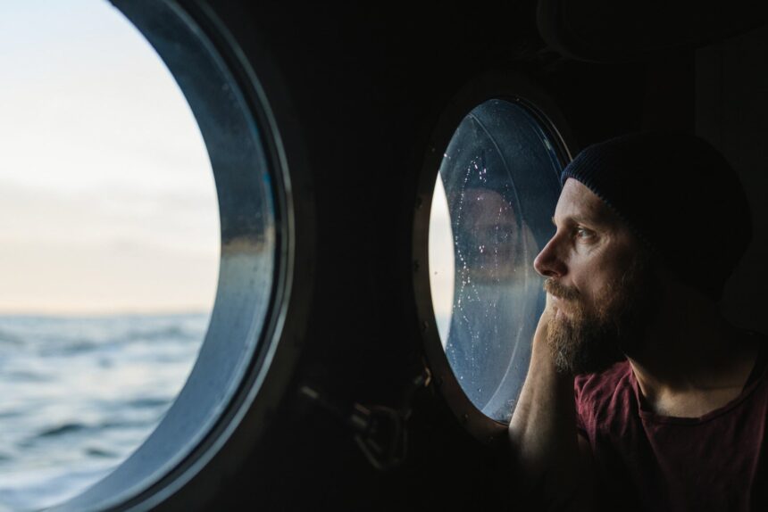 Man at the porthole window of a vessel sailing the ocean