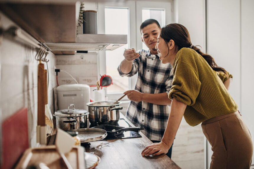 Two people in the kitchen at home. Husband is cooking for his wife, wife is tasting it.