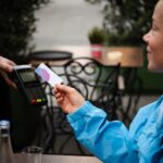 Happy young woman paying for her coffee by a credit card