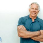 Mark stands smiling with arms crossed in front of white background with text "Primal Health Coach Institute."