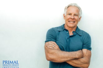 Mark stands smiling with arms crossed in front of white background with text "Primal Health Coach Institute."