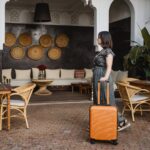 side view of young woman with an orange suitcase in the hotel