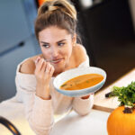 Picture of young woman tasting pumpkin soup in the kitchen.