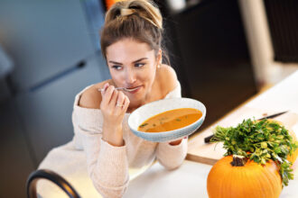 Picture of young woman tasting pumpkin soup in the kitchen.