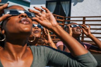 Women friends at home enjoying solar eclipse looking at the sun with eclipse sunglasses