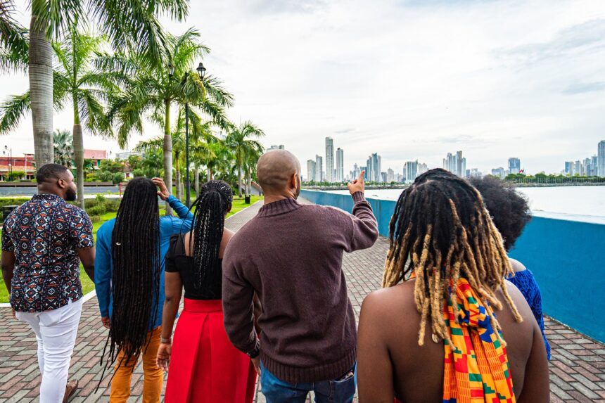 Local Tour Guide Walking and Pointing Toward the Skyline with a Group of Cheerful, Fashionable Afro-Descendant Tourists Together with a View of Panama City