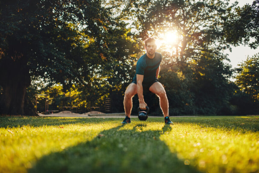 Full length portrait of fit young man training with kettlebell in the park.