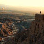 Woman standing on Font's Point looking at hot air balloons flying over badlands, Anza-Borrego Desert State Park, California, USA